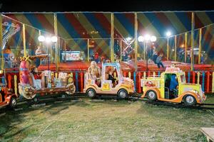 Little children ride in carriages on a toy train at an amusement park photo
