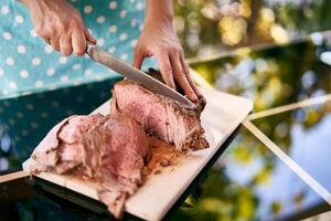 Housewife with a large knife cuts slices of juicy roast beef on a cutting board on a mirror table photo