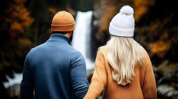 A couple holding hands while standing in front of a majestic waterfall photo