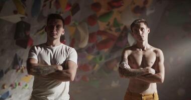 Determined coach and wall climber with hands folded in gym video