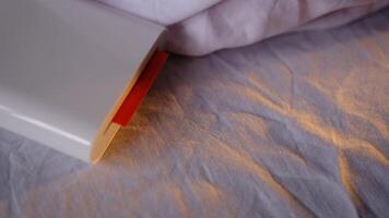 A compact pocket-sized white printer on bed prints polaroid style photo with orange colour in minimalist design modern technology creative process cozy atmosphere vibrant details portable convenience video
