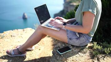 Freelance woman sea. working on a laptop by the sea, typing away on the keyboard while enjoying the beautiful view, remote work. video
