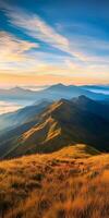 Stunning mountain landscape at sunrise with rolling hills and vibrant sky. golden grass contrasts beautifully with blue mountains in background, creating serene atmosphere photo