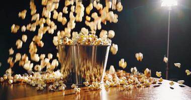 lot of popcorn pours into a large bucket on a table in the light of spotlights on a dark background. video