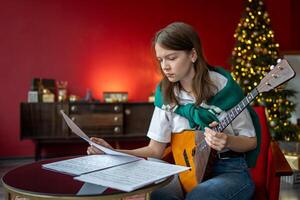 Focused woman studies balalaika song, read sheet music. Christmas event preparation, song homework photo