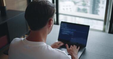 Rear view male 30s coding on laptop screen. Man look at laptop screen, hands coding and programming on laptop. Professional male developer programming apps doing project tasks sitting in modern office video
