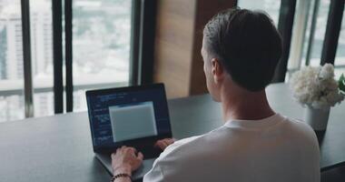 Software engineer at work as he skillfully crafts code on his laptop, providing an inside look at programming in action. Programming Professional, Man Crafting Code on Laptop Seen from the Back video
