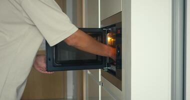 Man reheating leftover meal using kitchen appliance, appliance offering effortless time-saving benefit in minimal space, appliance enhancing daily routine, perfect for modern living visuals. video