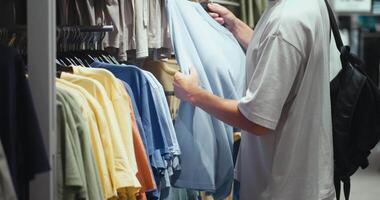 Man checking t-shirts in store, store boosting variety of casual apparel, store reflecting modern taste and diverse sizing, perfect for capturing daily shopping or brand marketing visuals. video