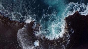 Powerful ocean wave crashes against rugged volcanic coastline, captured from above with swirling foam and turquoise water in a dramatic natural display video