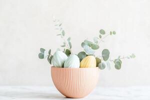 Minimalist Easter centerpiece featuring primitive patterned pysanka Easter eggs and eucalyptus leaves in a textured bowl on a marble countertop photo