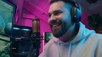 Carefree Caucasian man blogger gamer male laughing enjoying computer game online e-sport at home glad streamer vlogger playing gaming addiction vlog guy speaking microphone neon influencer stream blog video