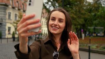 sonriente caucásico mujer hembra mujer de negocios negocio niña en ciudad calle fuera de participación móvil teléfono teléfono inteligente distante conferencia llamada grabar tomar imágenes selfie foto influencia ondulación Hola video