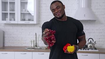 Black man holds out bunch of grapes. Black man holds out bunch of grapes while standing in the white kitchen video
