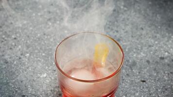 Red cocktail with a large ice sphere and lemon zest, smoke coming out when the wooden lid is removed video