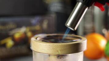 Professional chef preparing aromatic wood chips, igniting smoke producing chips in transparent glass container using culinary torch and sealing with lid video