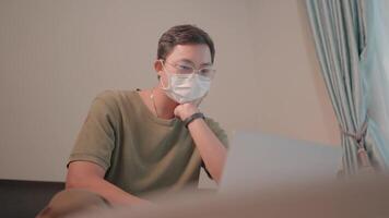 Working from Home with a Mask.A focused individual wearing a protective face mask intently views a laptop screen at home video