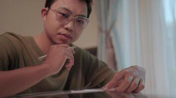 A determined young man studies the young man wearing glasses intently, thoughtfully reviewing notes and documents at his desk. This image represents dedication and the pursuit of knowledge. video