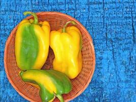 Three green and yellow peppers in a basket on a blue background video