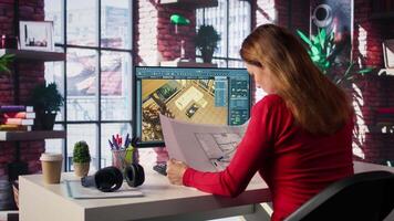 Freelancer designer decorates apartment floor plan using blueprints on pc, using architectural software to configure elements. Woman uses interface to enable rendering and 3D modeling. Camera B. video