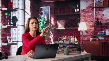 Focused remote worker swipes AI hologram visualization at her home office, looking at the holography projection in her modern loft. Woman utilizing artificial intelligence. Camera B. video