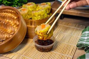 Hand holding dim sum with chopsticks and dipping it in chili oil. A traditional Chinese food. photo