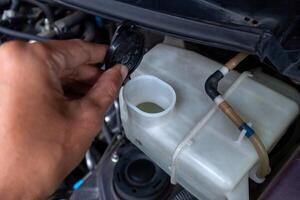 A mechanic's hand checking a tube of car window washer fluid. Open the cap on the wiper fluid tube for the windshield. photo