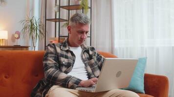 Man working on laptop computer with pensive expression, pondering a solution answer at home room video