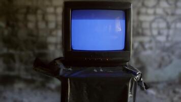 Old television set showing a blue screen with interference and turning off progressively, placed on a black plastic bag in an abandoned place video