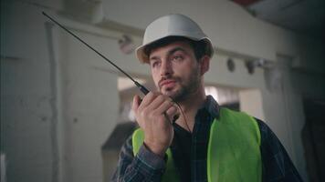 Serious Caucasian man worker executive guy builder mechanic talking walkie talkie architect male ordering architectural project in factory controller speak construction engineer control manufacturing video