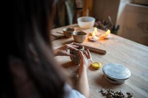 Female ceramist molds clay cup with decorative pattern on wood table in workshop. DIY, master class photo