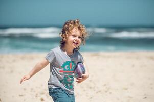Cheerful boy with ball walking on beach photo