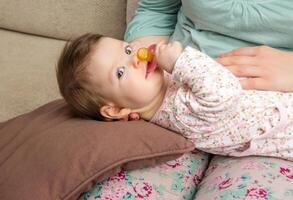 Baby playing with pacifier lying over mother legs photo