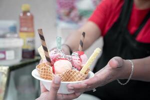 An adult Hispanic woman is serving a traditional Mexican ice cream with toppings to a client photo