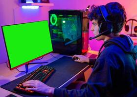 Caucasian young teenager plays computer in his room with colored lights and looks at the screen concentrated photo