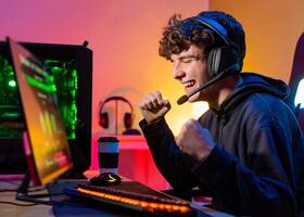 Young teenager plays the computer and celebrates victory in game with a clenched fist and a smile. photo
