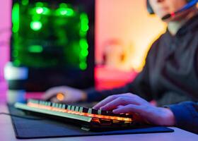Unrecognizable young gamer with hands on illuminated keyboard in room with colored background photo