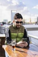 A smiling man sending messages while smiling at a bar near the river photo