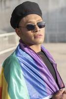 Gay man with make up on under LGBT rainbow flag while looking at camera. Concept of Pride. Pride month. photo