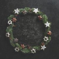Christmas circle frame made with fir wreath and cookies on dark concrete kitchen table. Christmas background with copy space. Top view. photo