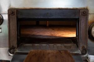 Wooden shovel set in front of a bakery stone oven open door with light inside photo