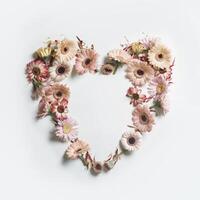 Heart frame made with various garden flowers at white background. Romantic concept with spring and summer petals for Valentine or Mother day. Top view. photo