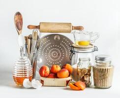 Baking setting with apricots, kitchen utensils, tools, honey and ingredients at white background. Baking with seasonal fruit at home. Front view. photo