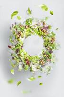 Circle frame of flying healthy green salad with lettuce, nuts, beans, dressing and vegetables. Balanced vegan food with copy space. Levitation of food photo