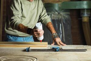Crop carpenter gluing wooden board in workshop photo