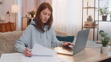 Focused woman freelancer reading documents and using laptop computer at table in living room at home video