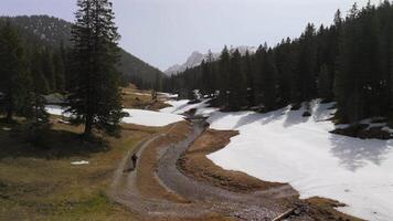 Man cycling on mountain bike along scenic trail in Austria or Germany. Surrounded by melting snow, rivers, and streams, with footbridge and cabin near mountaintop plateau. Spring in the mountains. video