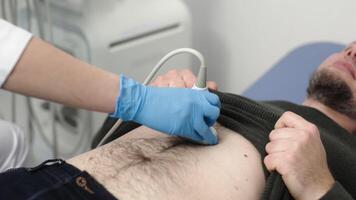 Close-up of practitioner examines with ultrasound of internal organs of middle-aged man in clinic. Ultrasound of abdominal cavity procedure concept video