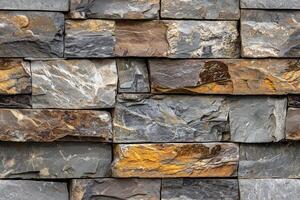 Textured artesia stone cladding wall made of various slate stones in shades of gray, brown, and gold. The stones are arranged in a staggered pattern, showcasing their natural colors and textures. photo