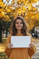 A smiling young woman holding a blank sign in the fall photo